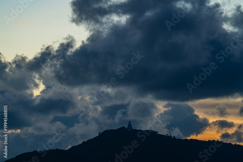 The golden sun sets behind the mountain casting a warm glow around the grand Big Buddha of Phuket. Silhouetted against a radiant sky, the sacred statue radiates peace and spiritual serenity.
