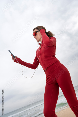 Female Runner on a Beach Wearing Red Activewear with Headphones and Smartphone