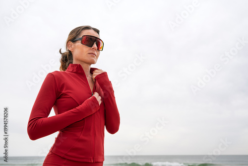 Fit Woman Athlete In Red Jacket And Sunglasses Training Outdoors on a Beach