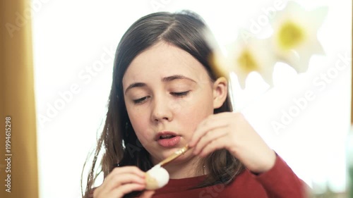 Little girl painting Easter eggs at home, 4K 10-bit cinematic footage of child decorating colorful eggs with watercolor brush for spring holiday, authentic lifestyle.