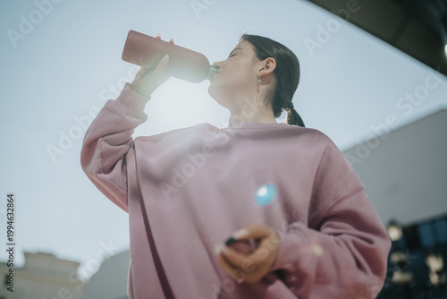 фотографія Young woman drinks from a reusable water bottle while standing outdoors
