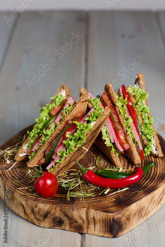 Tableau sur toile Fresh club sandwich with ham vegetables on rye bread served on rustic wood