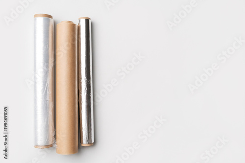 Cling film, aluminum foil, parchment paper on gray background flat lay top view. Kitchen rolls for packaging and storing food