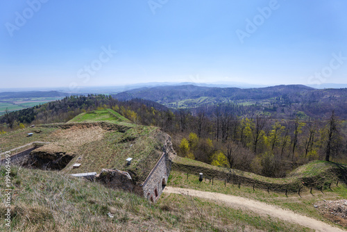 View of mountains and valleys from a hilltop with old structures during a clear daylight in springtime in a rural area. Srebrna Góra Fortress, Poland