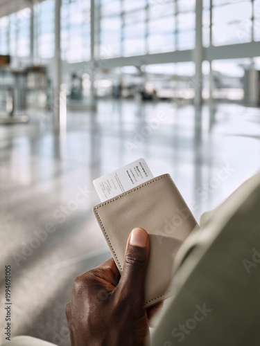A person's hand holding a boarding pass in an airport terminal.