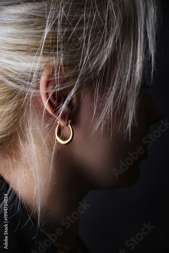 Side profile of blonde woman with elegant gold hoop earring, soft lighting, minimalist style