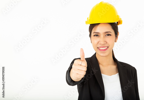 Portrait Pretty Asian Architect Woman with black suit and yellow safety helmet show her thumbs up in approval, give permission, recommend construction company, isolated over white background