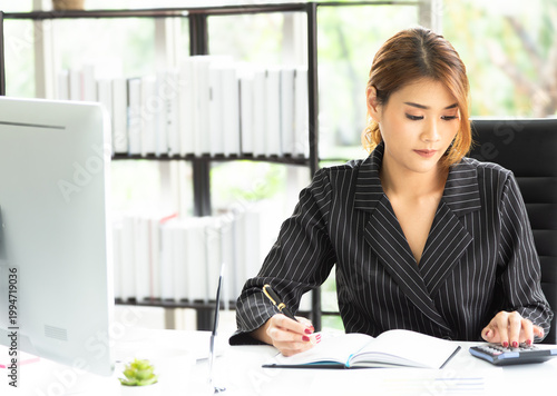 Beautiful business woman in black suit sitting and working in modern office and using digital tablet for online conference and business. Technology, internet, investment and stock market concept.