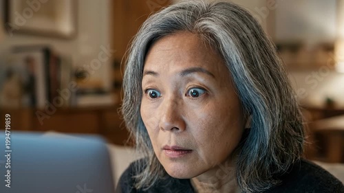 Mature woman reacts with surprise while looking at a laptop at home. Close-up captures shock, concern, and curiosity, suggesting unexpected news, online discovery, or financial alert.
