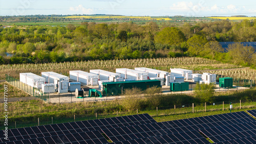 Aerial view of Tiln Photovoltaic Solar Farm and Battery Energy Storage System with white storage containers and solar panels surrounded by lush green trees in Retford, England, United Kingdom.