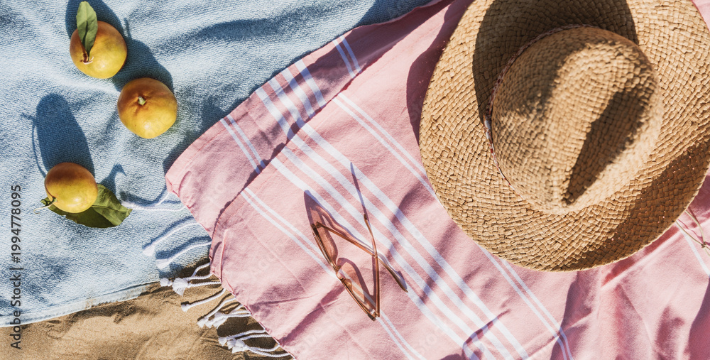 Naklejka premium Summer beach accessories flat lay on sand background. Holiday travel, tropical concept. Straw hat, sunglasses, towel and fruits. Sun shadow and sunlight