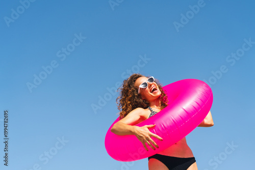 Obraz na plátně Joyful woman having fun with pink floaty on summer beach