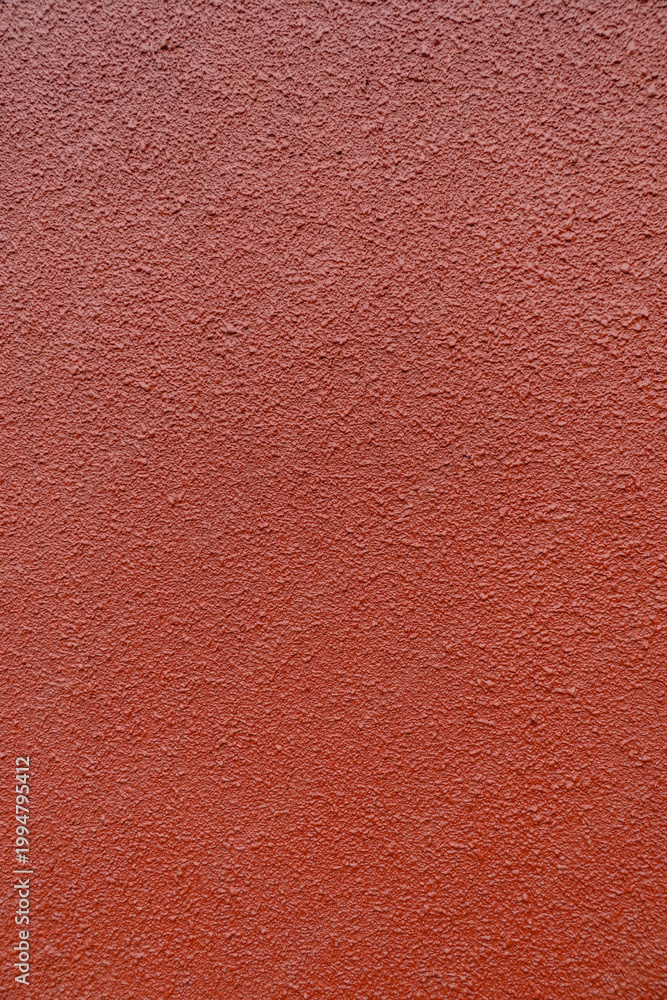 Fototapeta premium Red textured wall surface with rough stucco finish, abstract background for design, construction, and copy space