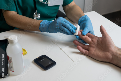Obraz na płótnie A nurse wipes a patient's fingertip with an antiseptic swab in a clinical setting before performing a prick