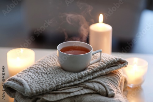 Warm Cup of Tea on a Cozy Blanket Next to Glowing Candles in a Relaxed Indoor...