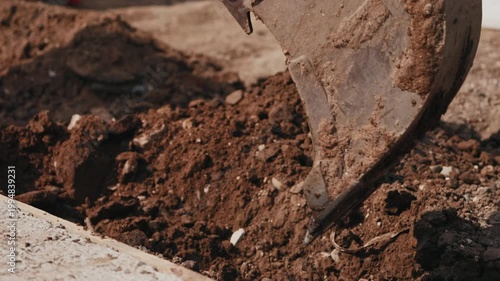 Excavator bucket digging soil in trench during construction close up
