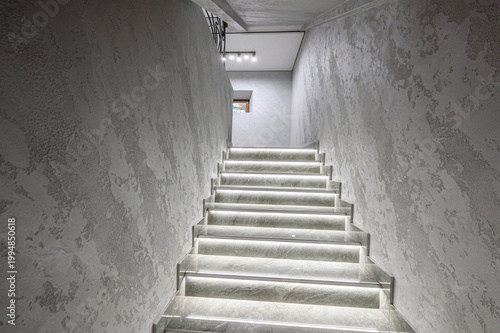 Photography Sleek modern staircase with illuminated steps, textured grey walls, minimalist design, LED backlighting, polished stone finish, narrow corridor, contemporary aesthetic
