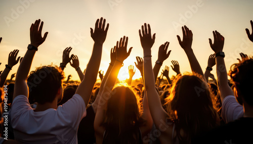 A crowd of people raise their hands in the air during a sunset. The people in the crowd seem engaged and energized as the sun sets behind them.