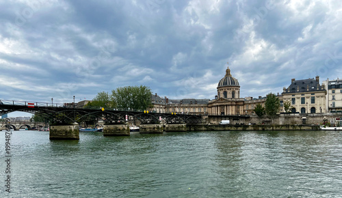 Pont des Arts bridge across the Seine River in Paris under dramatic cloudy skies with the Institut de France in the background.