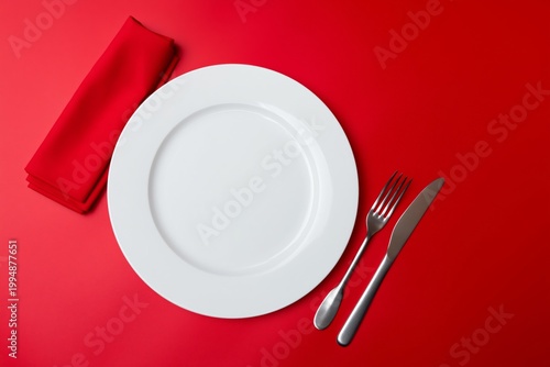 Table Setting With Silverware and Empty Plate on Bright Red Background During...