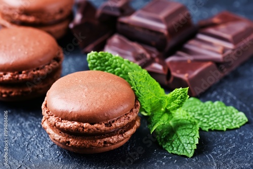 Chocolate Macarons With Mint Leaves and Dark Chocolate Pieces on a Dark Surface