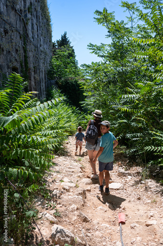 Active recreation with children. A family walks along a green path through trees near old ruins. Hiking in the mountains. 