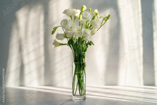 White Flowers Are Arranged in a Clear Vase on a Table With Light and Shadow P...