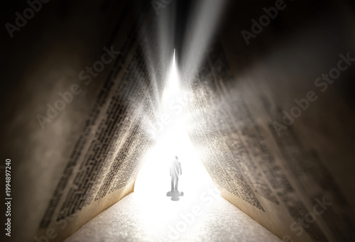 A silhouette of a man walking toward a bright light through a huge ancient book. The concept of religion, God, soul, faith, light at the end of the tunnel, freedom of choice, open mind, meditation.
