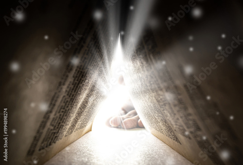 A huge human palm is visible through the open ancient book, illuminated by bright rays of light. The concept of religion, God, soul, faith, light at the end of the tunnel, freedom of choice, open mind