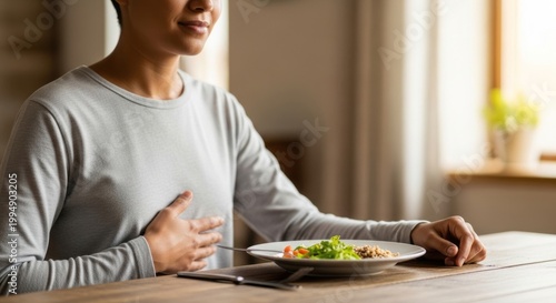 Woman practicing mindful eating by listening to her body signals at the dinner table. Concept of intuitive eating versus restrictive diet culture. Healthy relationship with food choice.