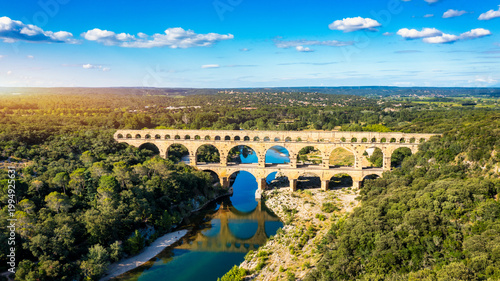 Aqueduct of Pont du Gard arches over the river, showcasing the rich history of Vers-Pont-du-Gard, France. Ancient aqueduct of Pont du Gard spans the peaceful river in Vers-Pont-du-Gard, France.