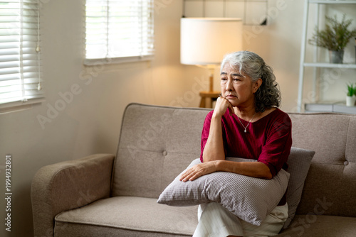 Sad Senior Asian Woman Sitting Alone on Sofa Looking Depressed and Lonely at Home