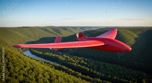 Red fixed wing drone flying above winding river in dense green forested mountain valley