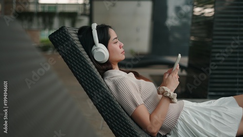 Fotografía Young woman listening to music via wireless headphones, sitting on cozy lounge c