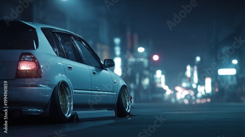 Modified hatchback parked on city street at night. Low rider car with custom rims and lowered suspension. Urban racing culture vehicle in rain with bokeh lights. Night driving atmosphere.