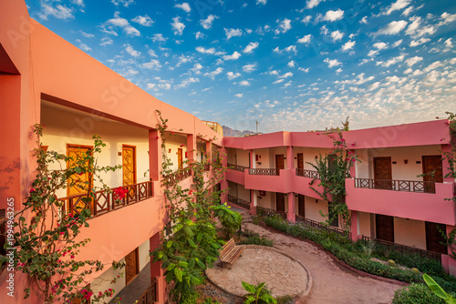 Horizontal wide-angle view of pink resort architecture with a courtyard garden and mountains in Dahab, Egypt.