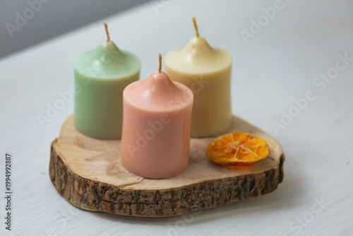 A collection of three colored harmony not burning design wax candles with dried natural orange in pastel soft colors in home interior. Closeup bath, care, spa, wellness, relaxation 