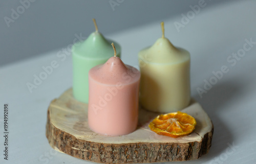 A collection of three colored harmony not burning design wax candles with dried natural orange in pastel soft colors in home interior. Closeup bath, care, spa, wellness, relaxation 
