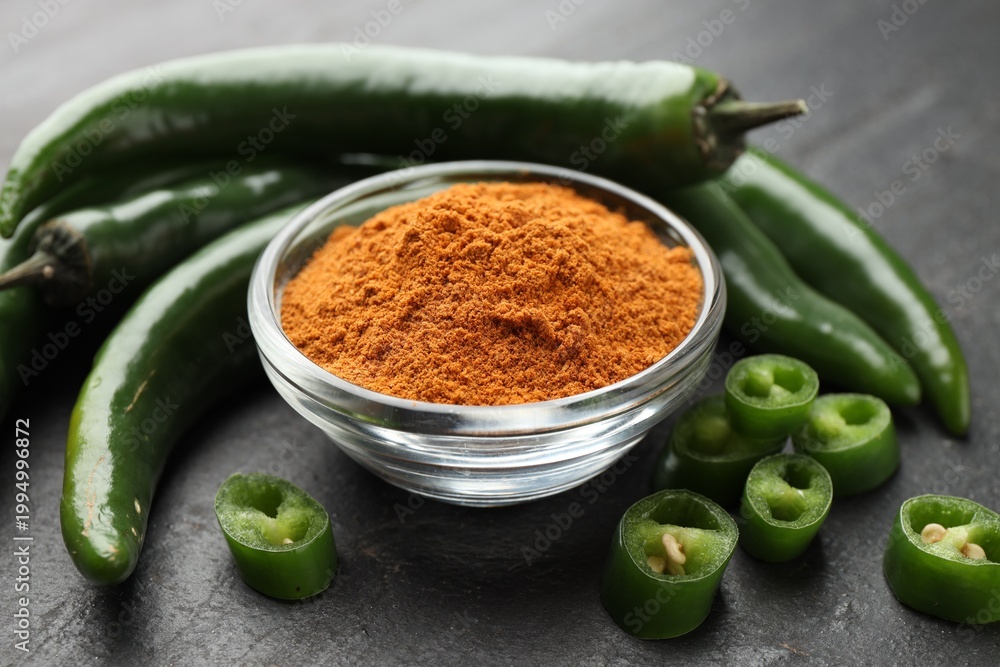 Fototapeta premium Powdered and raw chili peppers on black textured table, closeup