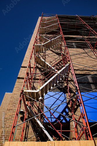 Metal stairway going to the top of scaffolding installed adjacent to building for window cleaning .