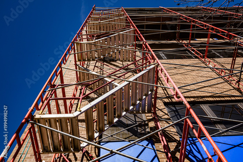 Metal stairway going to the top of scaffolding installed adjacent to building for window cleaning .