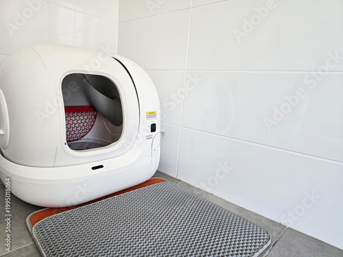 Modern automatic self-cleaning cat litter box placed on a tiled floor with a mat. Concepts of pet care technology, home convenience, and smart living solutions.