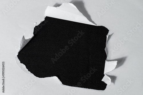 Fotografie A rough tear hole in the center of a white sheet of paper against a contrasting, solid black background