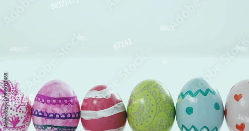 Displaying row of painted glossy eggs on white table with pale blue gradient and faint numbers