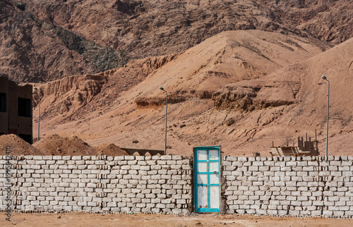 Solitary turquoise door in a white stone wall against desert mountains in Dahab, Egypt.