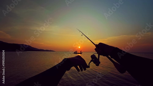 First person view of spinning rod directed toward horizon with small boat silhouette at sunset over sea, tranquil fishing scene and travel mood