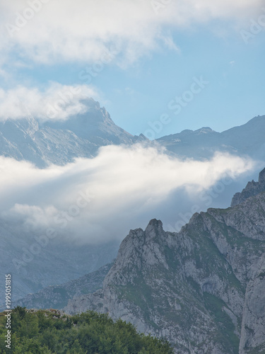 Rugged Limestone Peaks in Picos de Europa - Majestic and dramatic mountain landscape with jagged limestone peaks, green slopes, and clouds hanging low in Picos de Europa, Asturias, Spain.