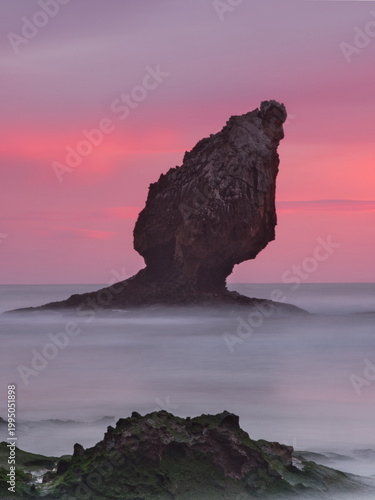 Dramatic Pink Sunset Sky over Buelna Stack - Spectacular long exposure of the iconic sea stack at Buelna Beach, Asturias, silhouetted against a vibrant magenta and pink twilight sky, with milky water.