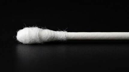 Single cotton swab with a fuzzy tip against a black backdrop, hygiene product close up, clean minimal composition with fine texture detail, sharp studio lighting, realistic presentation, no logos