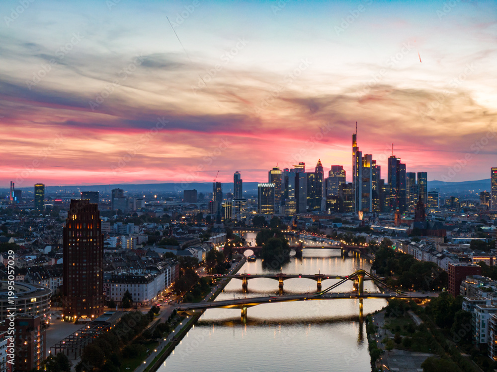 Naklejka premium Frankfurt skyline glowing over main river at sunset